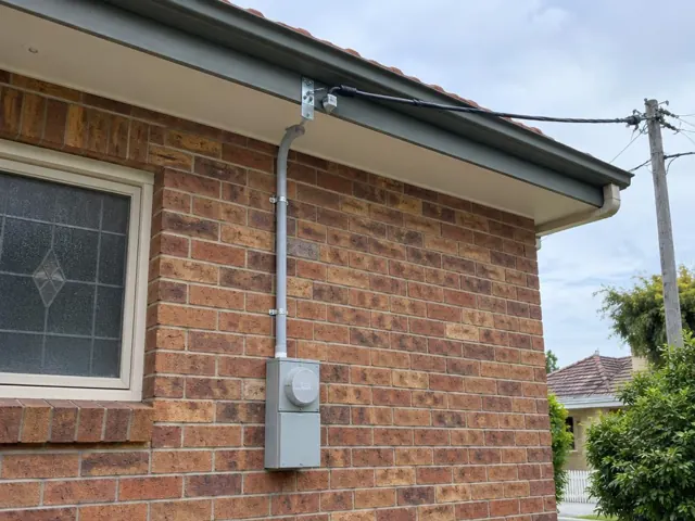 Brick house exterior with new overhead service cable and point-of-attachment bracket under the eaves in Waratah
